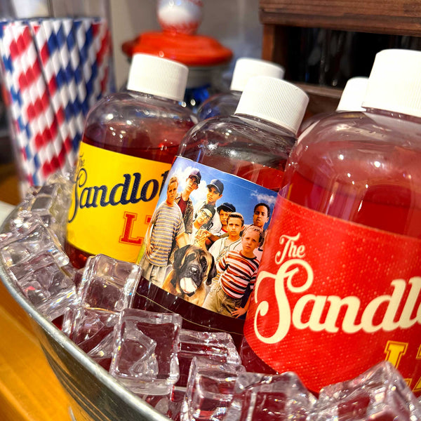 Three bottles of Sandlot lemonade on a tray with ice, surrounded by vintage-themed decor.