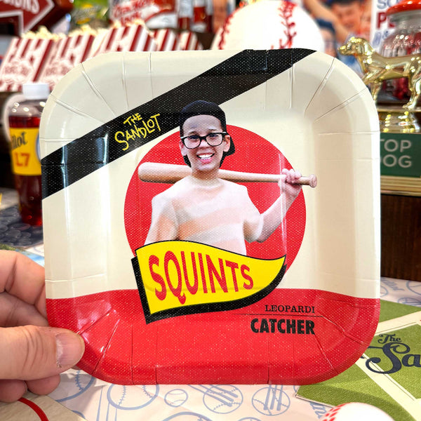 Paper plate with a humorous design of a person holding a baseball bat, featuring text and a red circle.