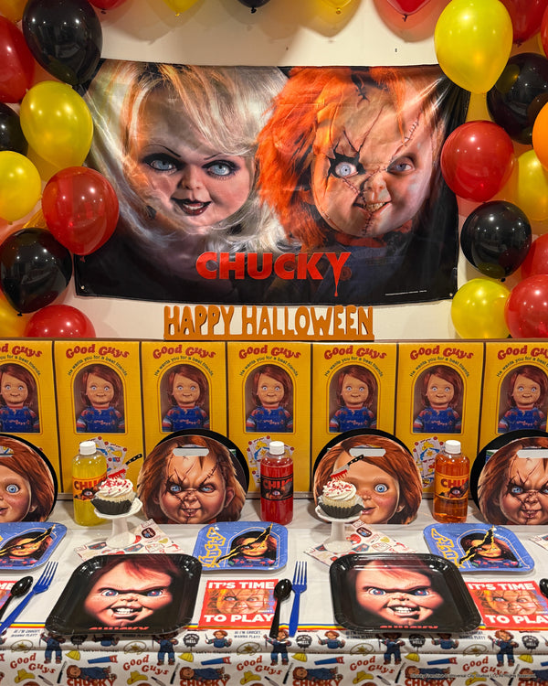 Chucky Halloween party table with a Happy Halloween fabric banner, red, yellow and black balloons, character plates and favor boxes