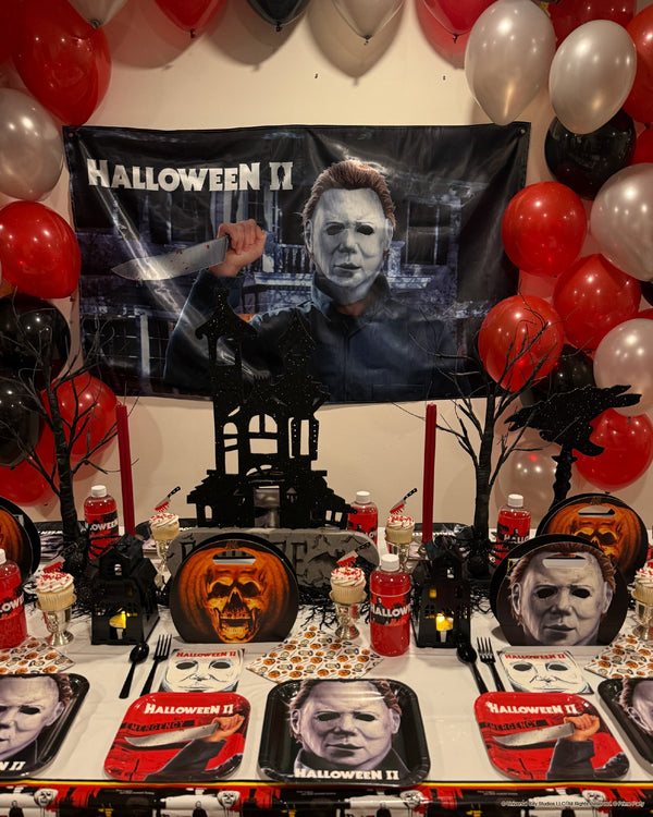 Halloween 2 party table set with a Michael Myers fabric wall banner, black and red balloons and a carved pumpkin
