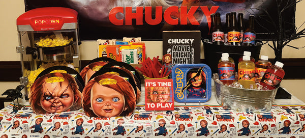 Chucky movie night concession stand with popcorn-filled character plates, theater candy boxes, red licorice and labelled bottles under a Chucky wall banner