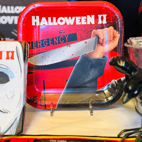A red Halloween-themed paper plate displayed on a stand, featuring the 'Halloween II' movie artwork with a hand holding a knife and the word 'EMERGENCY'.