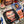 A themed Chucky party table setting featuring a black paper plate with a large Chucky face, a blue square plate with a smaller Chucky graphic, a cupcake with red sprinkles on a white pedestal, a red drink cup, and a printed tablecloth with Chucky character illustrations.