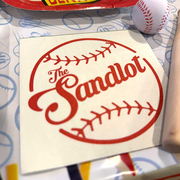 The Sandlot logo on a piece of paper with a baseball and baseball bat in the background.