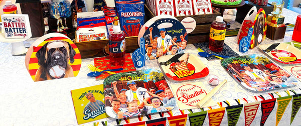 The Sandlot-themed baseball party table setup featuring officially licensed party supplies including plates, napkins, drink bottles, popcorn boxes, baseball decorations, trophy props, and character-inspired favor boxes. The colorful retro baseball party display includes iconic Sandlot imagery, a Beast dog decoration, mini baseball bat accents, and classic movie quotes, perfect for birthday parties, Little League celebrations, baseball watch parties, and 4th of July gatherings.