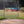 Birthday banner with a group of people displayed on a chain-link fence in an outdoor setting. Sandlot-themed birthday banner attached to a baseball field fence with kids and dog design and “You’re Killin’ Me, Johnson” text.