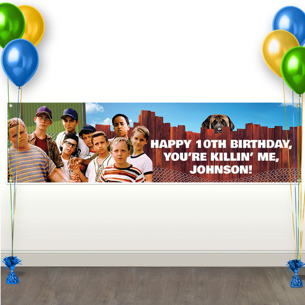 Sandlot-themed birthday banner with a group of boys standing by a fence and a dog peeking over, featuring the text “Happy 10th Birthday, You’re Killin’ Me, Smalls!” displayed on a wall with colorful balloons on both sides.